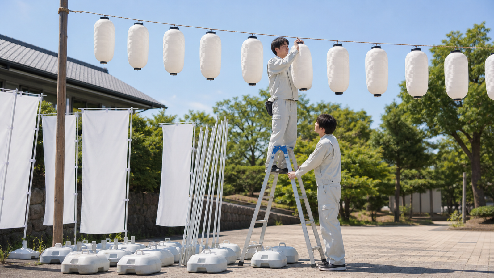 脚立に乗って連提灯を吊る設営スタッフと、注水台に立てたのぼり