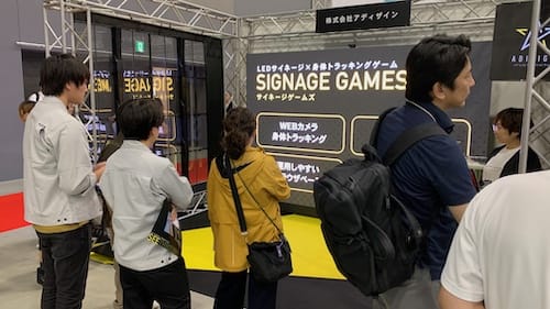 展示会ブースでWebカメラ連動の身体トラッキングゲーム「SIGNAGE GAMES」に来場者が集まっている様子