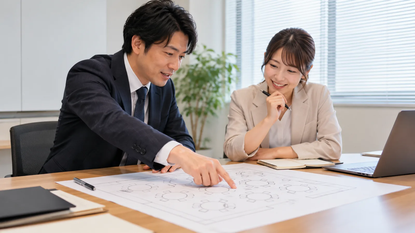 会議室のテーブルで、幹事の2人が会場の見取り図を広げて話し合っている様子を、横から写した写真